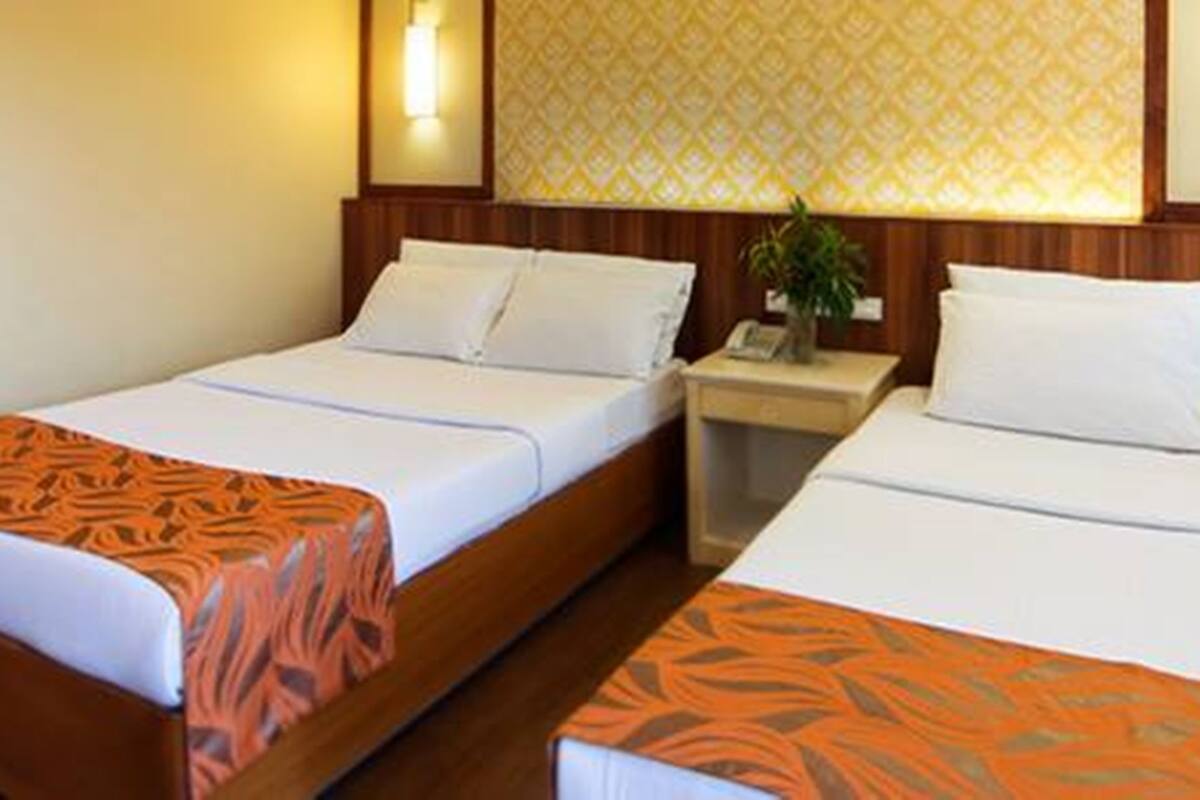 A hotel room with two single beds, a nightstand with a lamp, and a patterned wall.