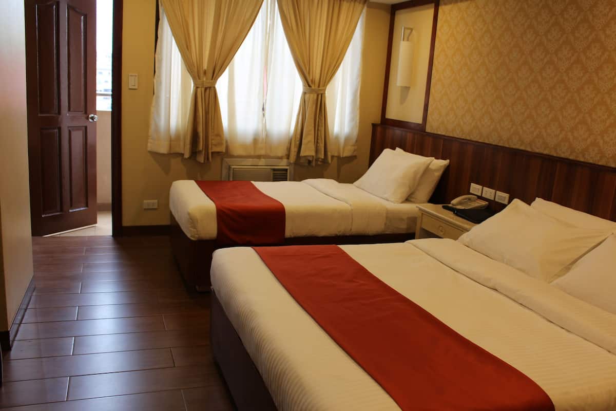 A hotel room with two beds, a wooden floor, a window with curtains, and a bedside table with a phone.