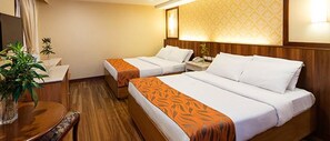 A hotel room with two beds, a wooden floor, a small table with a chair, and a potted plant. - Hotel Veniz Burnham (Baguio)