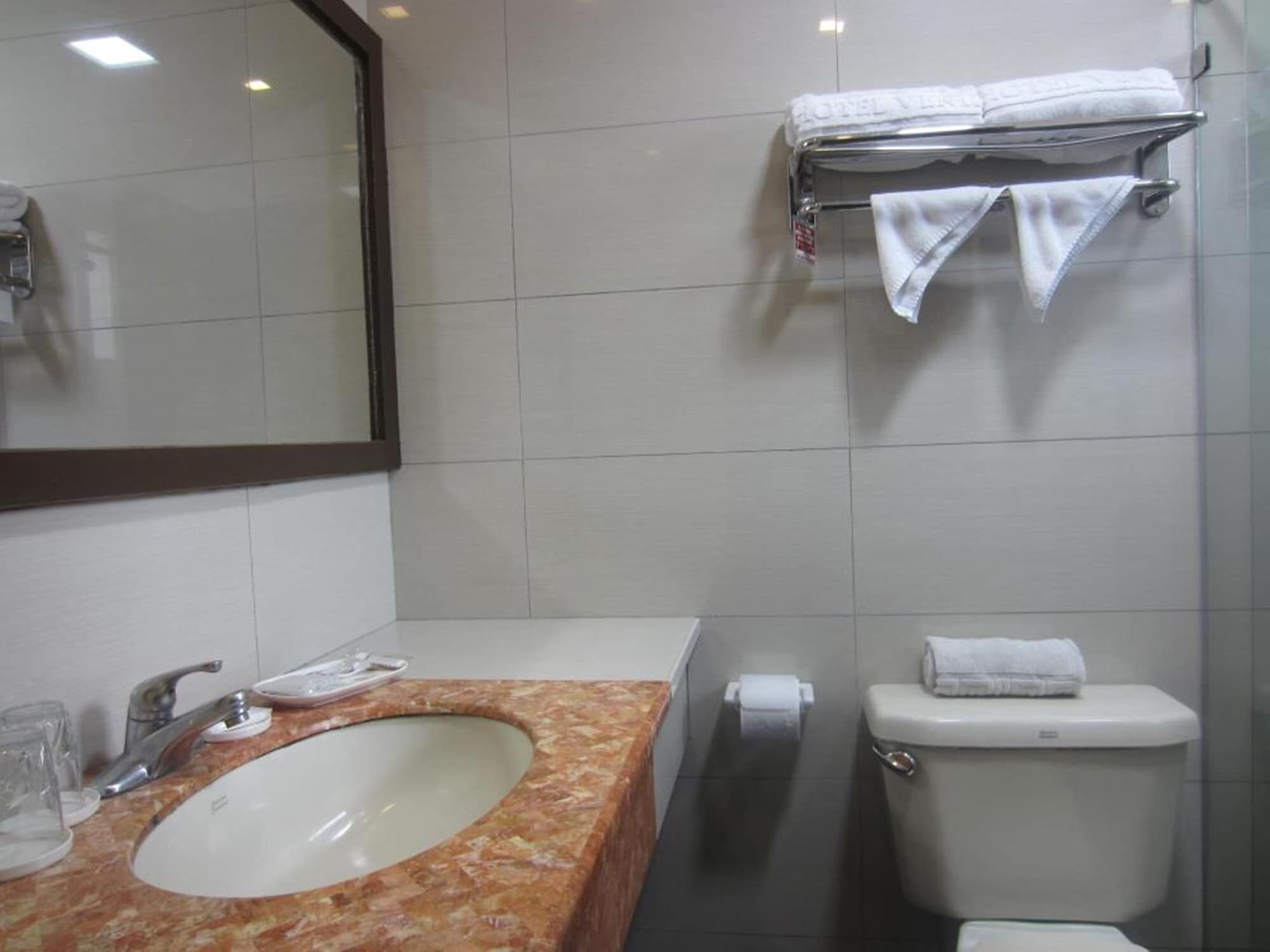 A bathroom with a marble sink, a mirror, a toilet, and a towel rack.