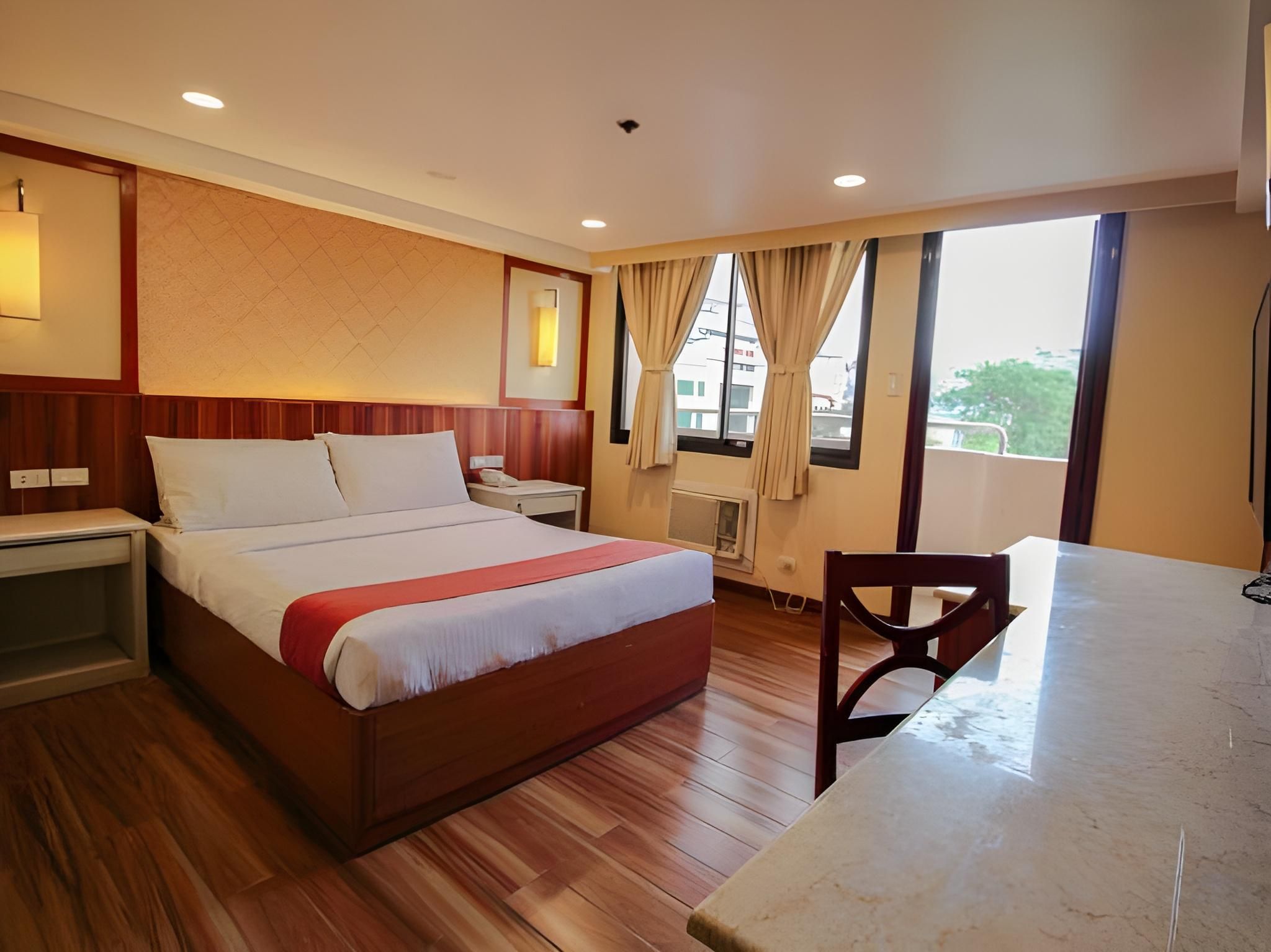 Una habitación de hotel con cama, mesita de noche, silla y vistas al exterior.