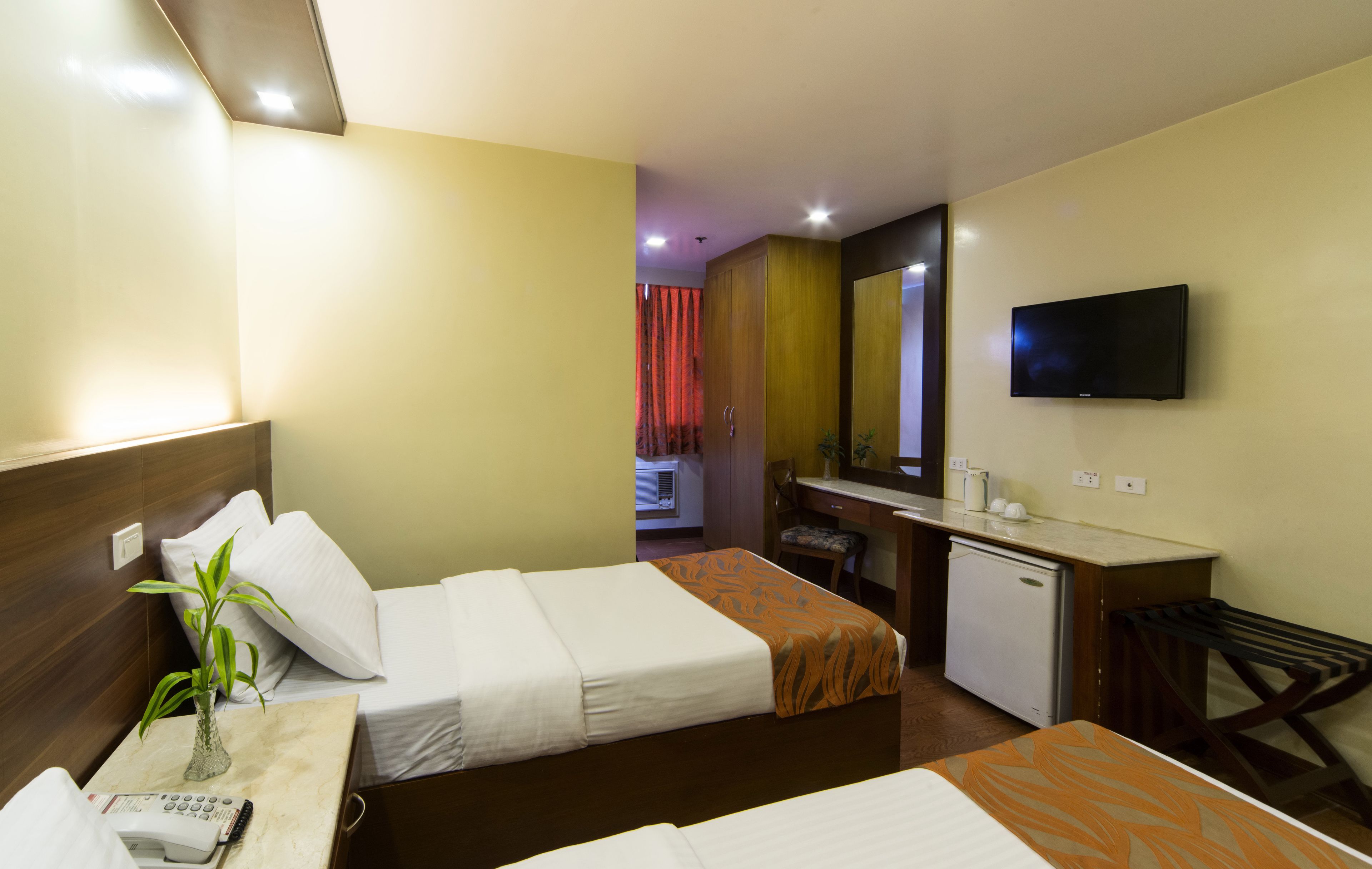 Habitación de hotel con dos camas, un escritorio con silla, televisor y una pequeña cocina.