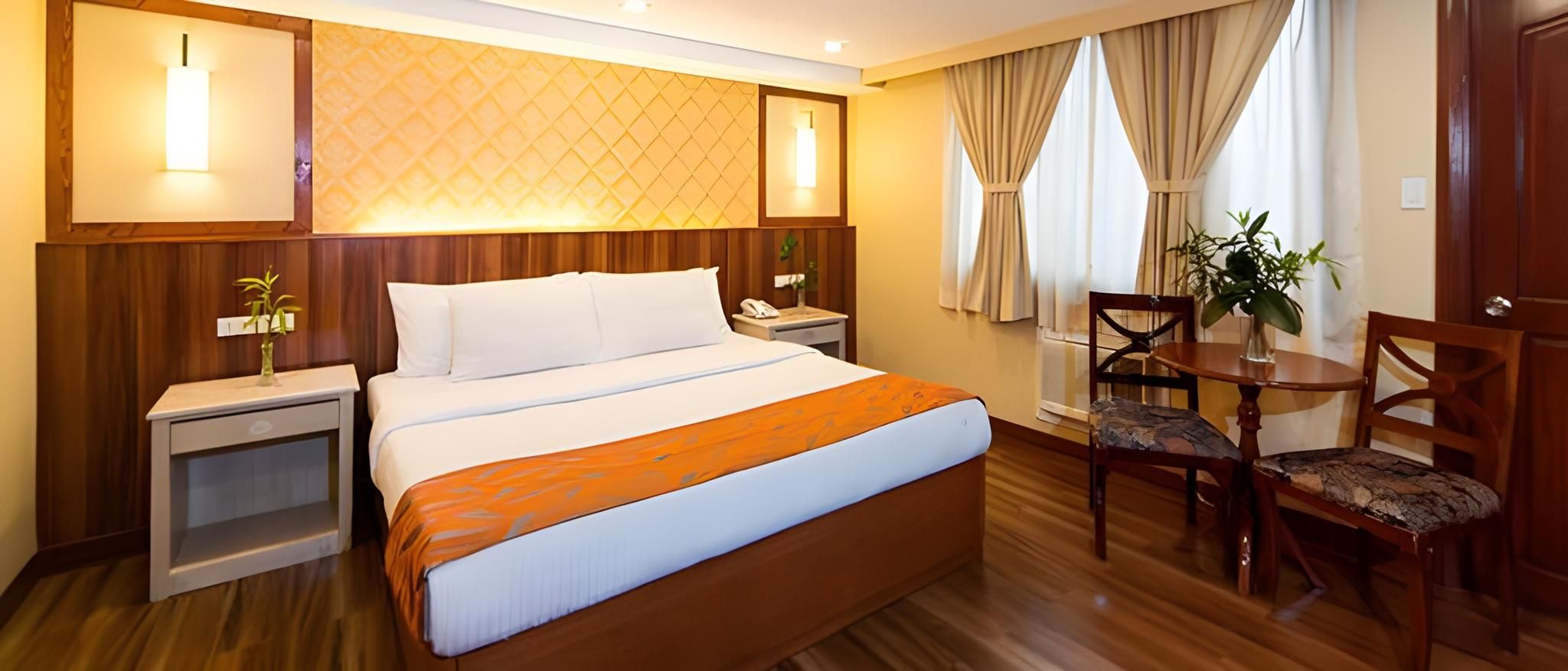 A hotel room with a bed, bedside tables, a desk with a chair, and a window with curtains.
