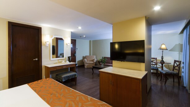 Una habitación de hotel con cama, escritorio, silla, sofá, televisor y lámpara.
