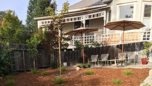 Een achtertuin met een houten terras, een patio met tuinmeubilair, en een huis op de achtergrond.