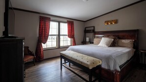 Un dormitorio con una cama grande, un banco, un aparador y una ventana con cortinas.