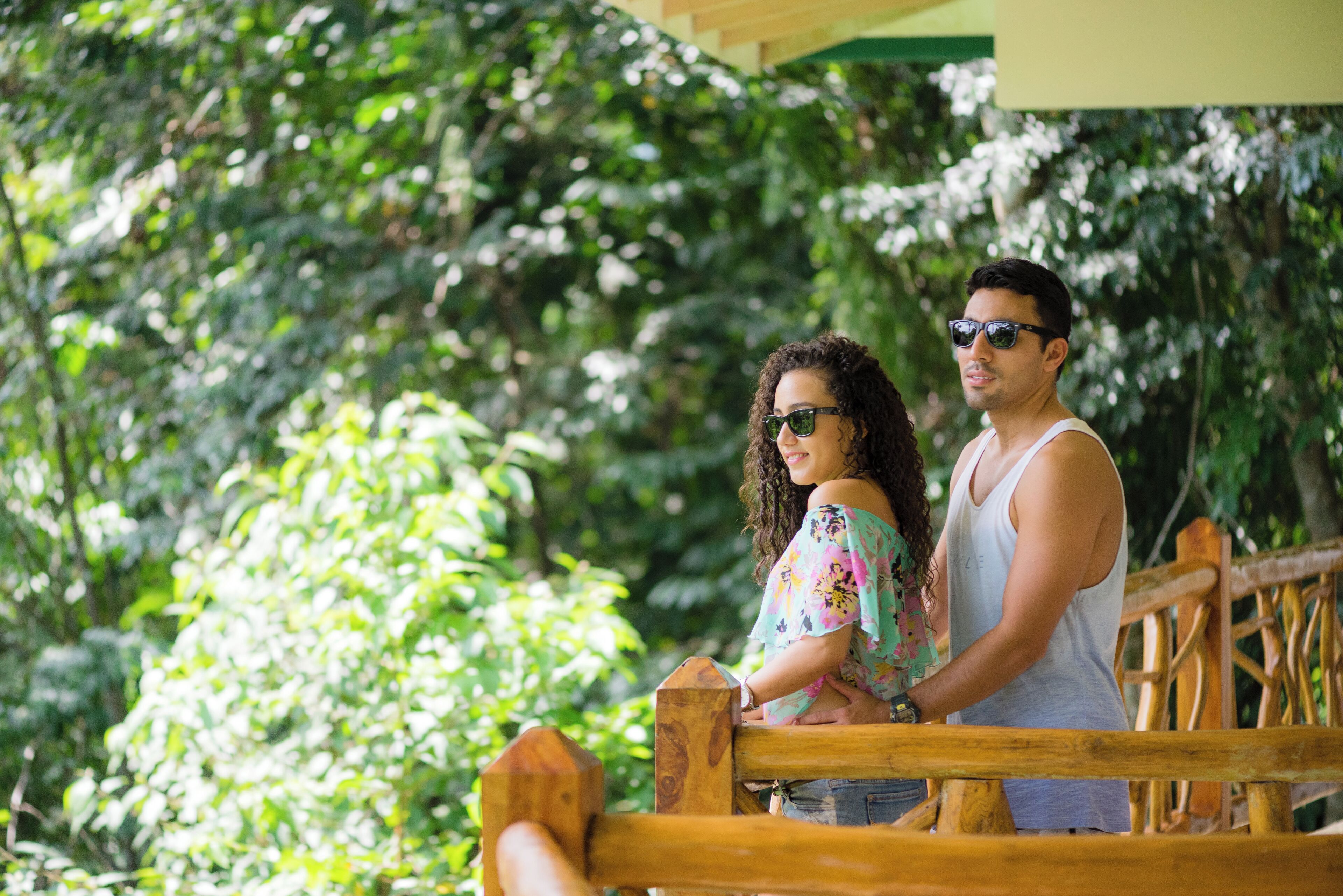 Two people standing on a wooden deck with lush greenery in the background.