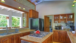 A modern kitchen with granite countertops, stainless steel appliances, wooden cabinets, and a large window overlooking greenery.