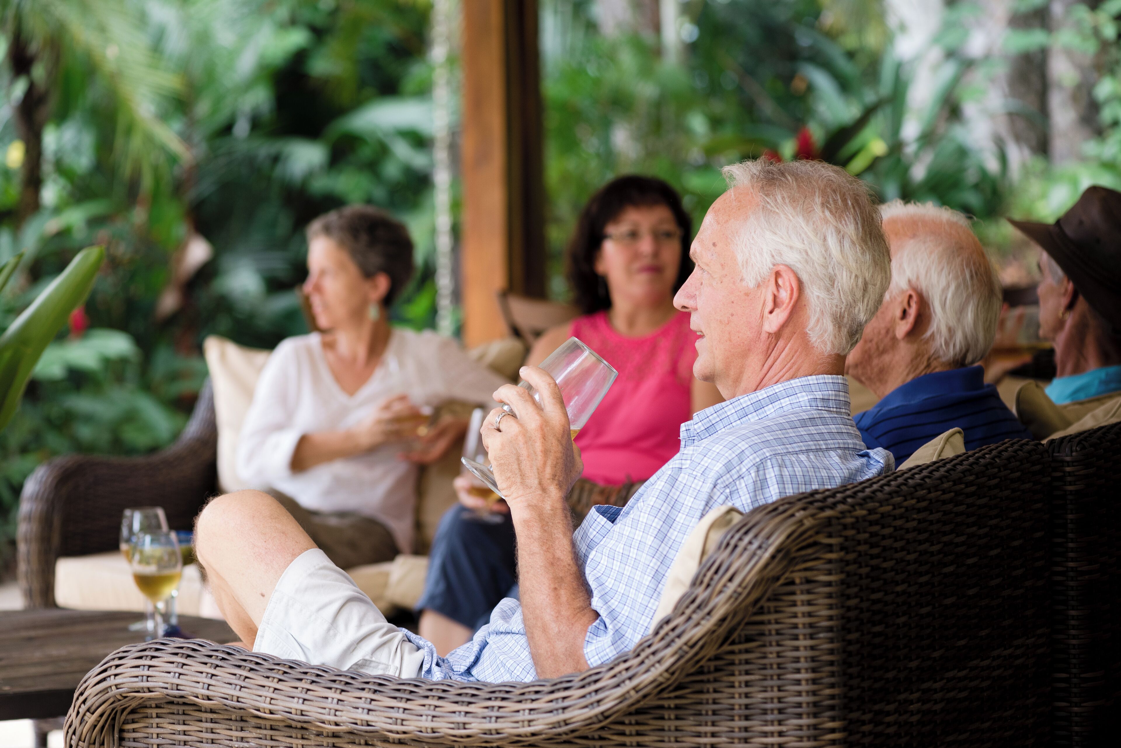 A group of people sitting on wicker furniture in a room with a view of greenery.