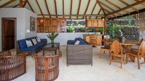 A covered outdoor living area with wooden furniture, a ceiling fan, and a stone wall backdrop.
