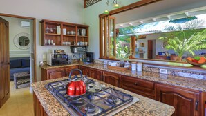 A kitchen with granite countertops, wooden cabinets, a red kettle, and a large mirror reflecting the outdoor view.