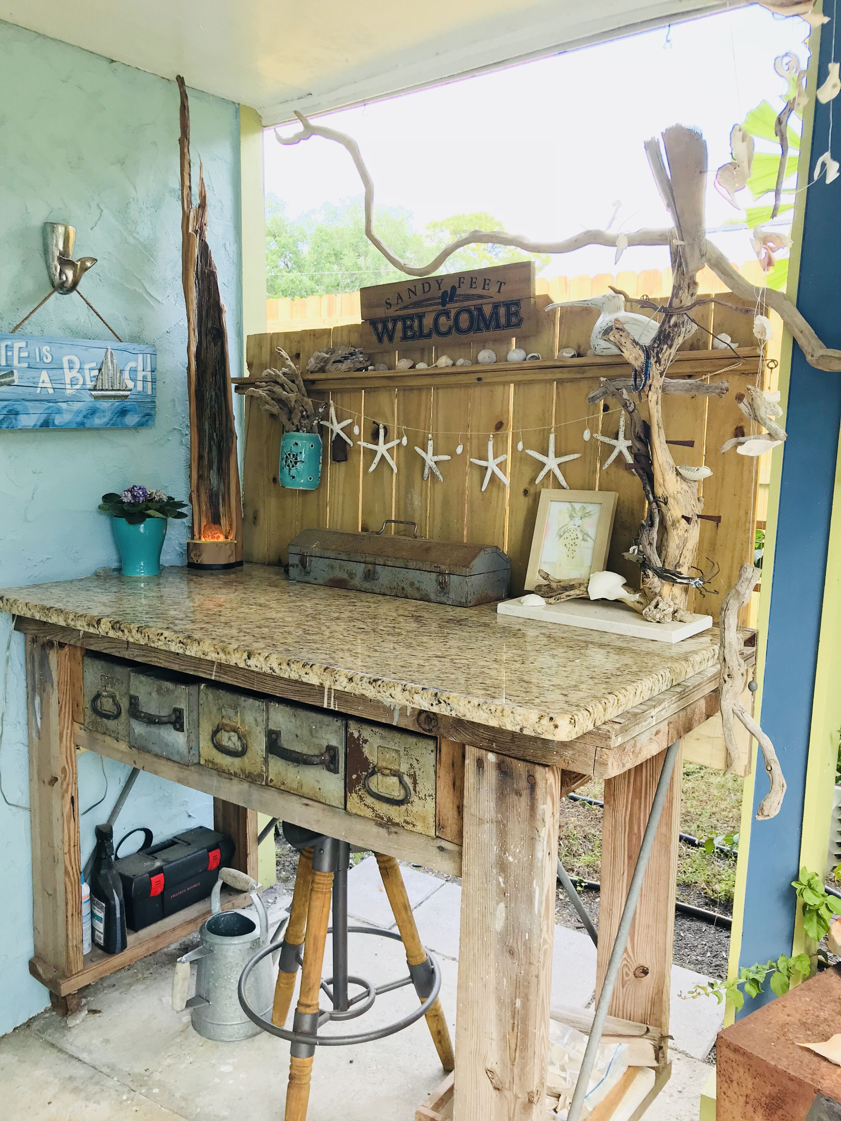A rustic wooden workbench with a 'Welcome' sign, starfish decorations, and a 'Coffee is a Beach' sign.