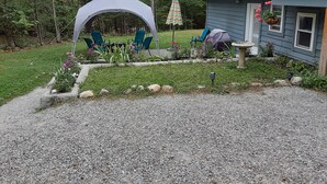 Zona d'estar a l'aire lliure amb seients i taula, envoltada d'un jardí amb pedres i plantes.