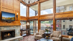 A spacious living room with a stone fireplace, comfortable seating, a television, and large windows offering a view of the surrounding area.