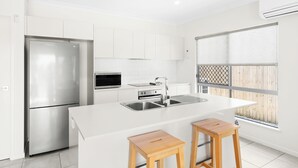 Una cocina moderna con armarios blancos, un refrigerador de acero inoxidable, horno integrado y una isla grande con taburetes.