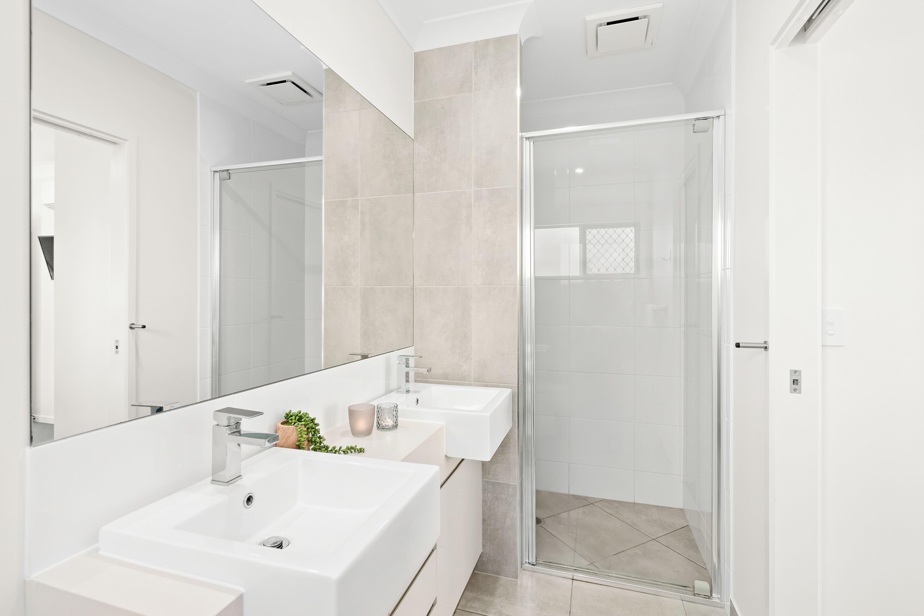 A modern bathroom with two sinks, a large mirror, and a glass shower enclosure.