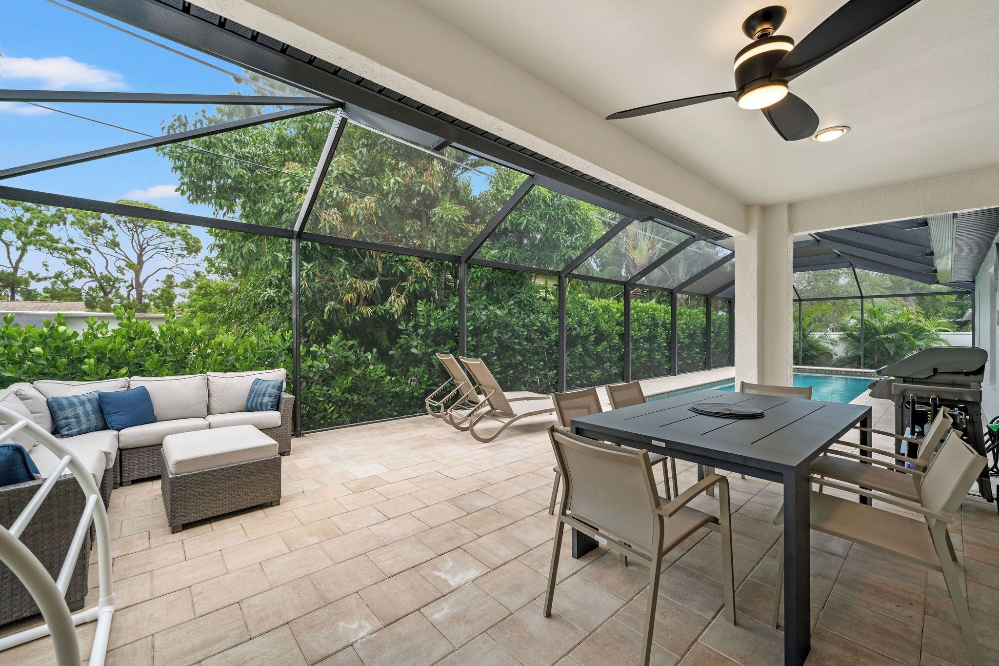 Eine Terrasse im Freien mit Glasveranda, einem Esstisch, Stühlen, einer Couch und einem Grill.