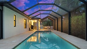 Una piscina interior moderna con techo de cristal, un área de descanso con asientos y vistas a la vegetación circundante.