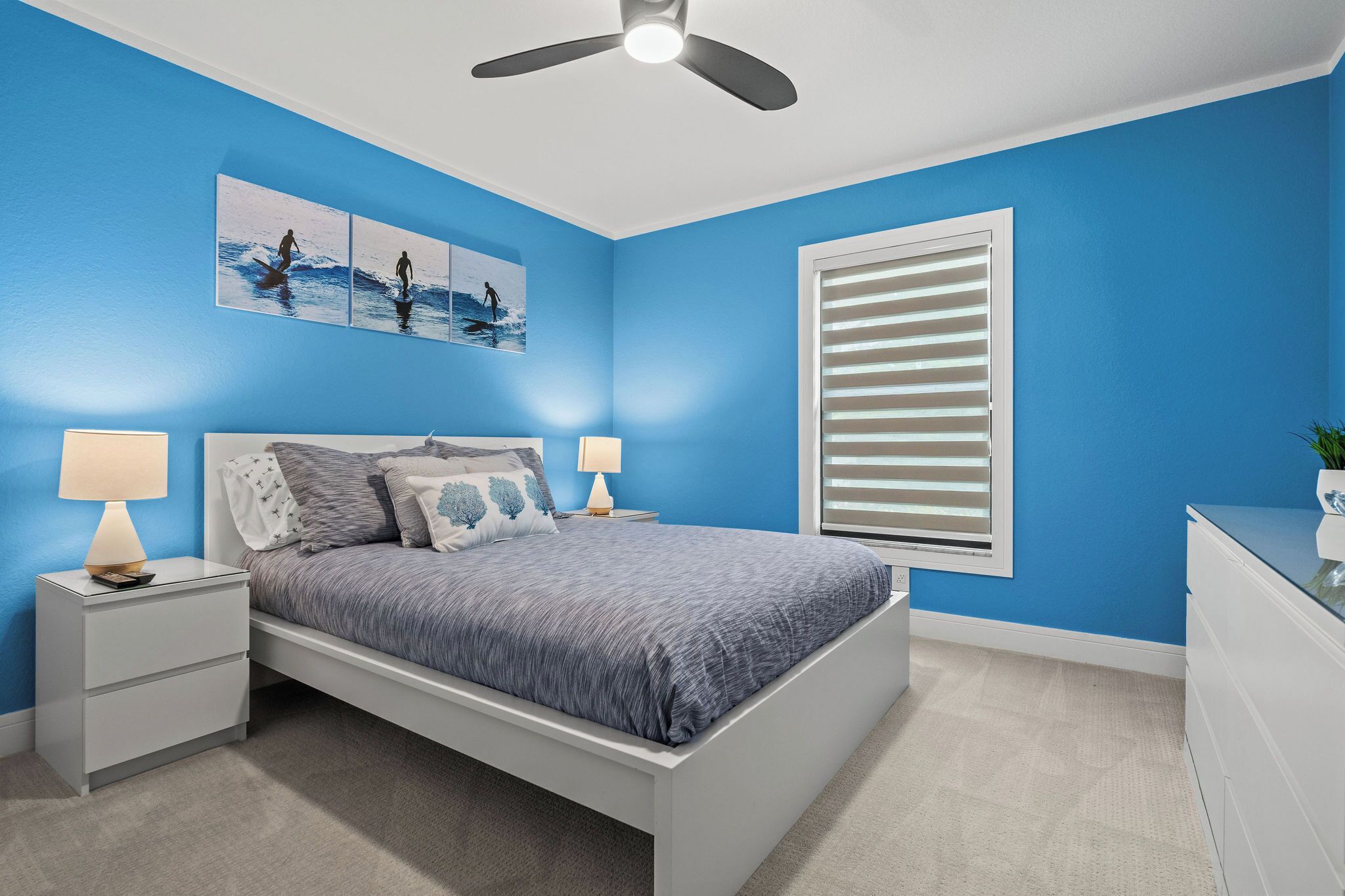 A bedroom with a bed, two bedside tables, a ceiling fan, and a window with blinds.