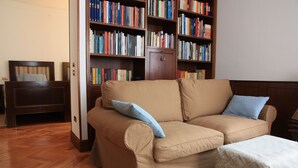 A living room with a beige sofa, two blue cushions, a wooden bookshelf filled with books, and a wooden cabinet.