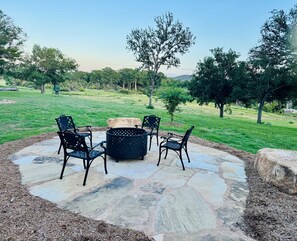 Une terrasse extérieure avec un sol en pierre, quatre chaises et un foyer.