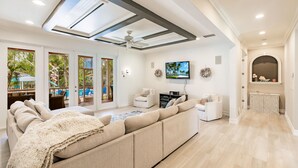 Un salon spacieux avec un grand canapé d’angle beige, un ventilateur de plafond et un téléviseur fixé au mur.