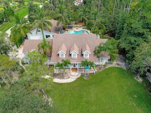 A large house with a swimming pool, surrounded by lush greenery and palm trees.
