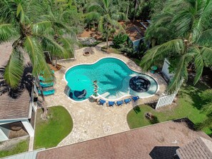 An aerial view of a swimming pool surrounded by palm trees and a brick patio area with lounge chairs. - Key West Style Luxury Home with resort heated saltwater pool & infinity line spa (Naples)