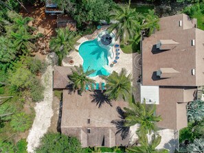 An aerial view of a residential property with a swimming pool, palm trees, and a brick-roofed house. - Key West Style Luxury Home with resort heated saltwater pool & infinity line spa (Naples)