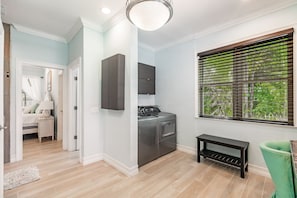 A laundry room with a washer and dryer, a bench, and a window with blinds.