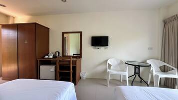 Habitación de hotel con dos camas, un escritorio con televisor, un espejo y un refrigerador pequeño.