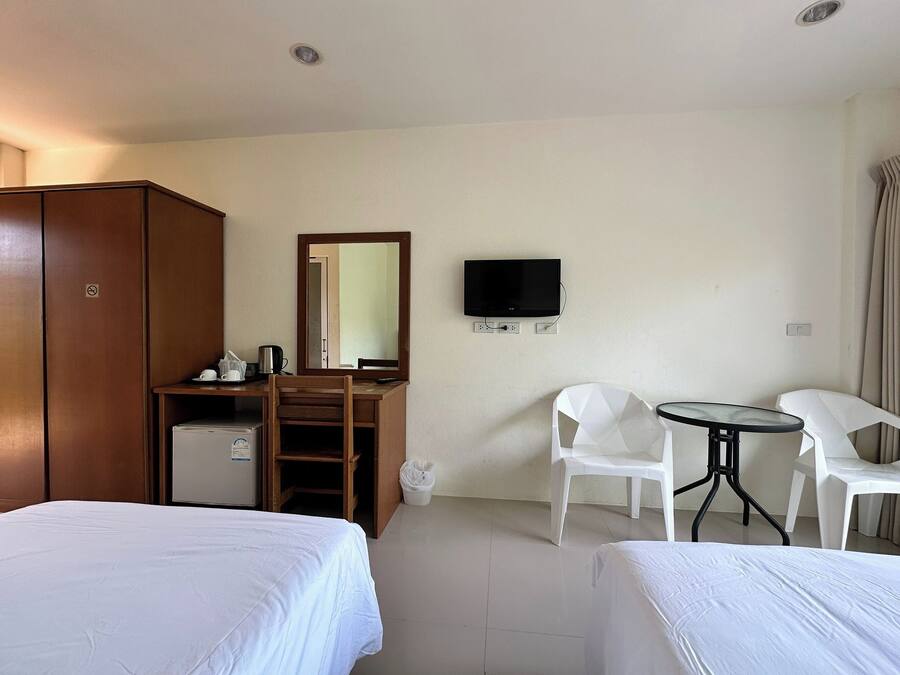 Habitación de hotel con dos camas, un escritorio con televisor, un espejo y un refrigerador pequeño.