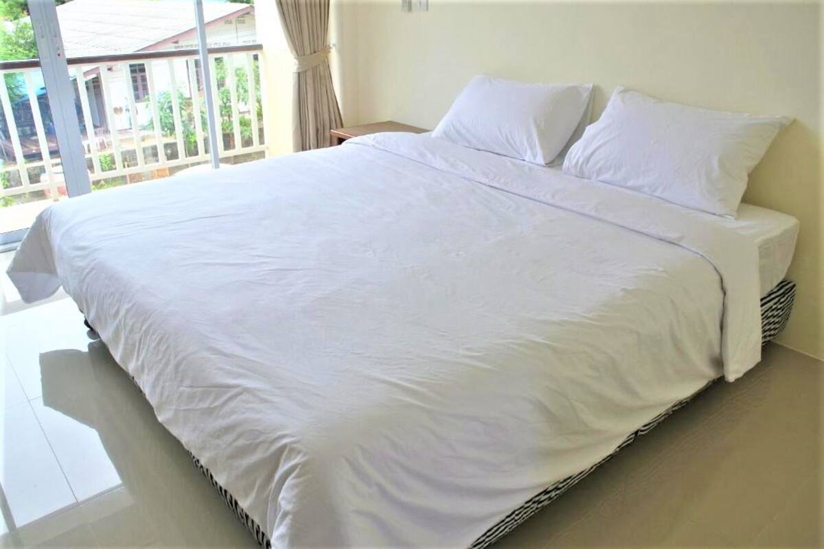 A large bed with white bedding in a room with a view of a house through a window.