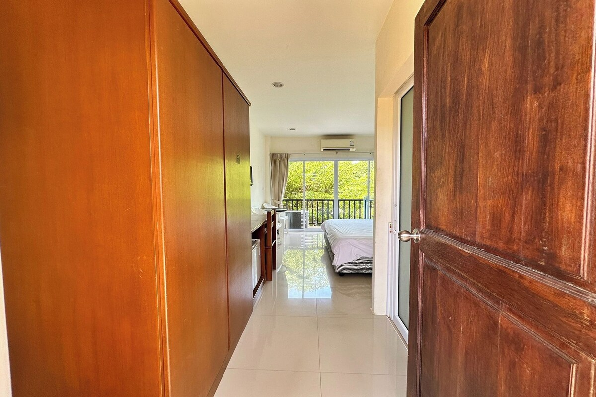 Un pasillo que conduce a un dormitorio con balcón, un baño y una zona de cocina.