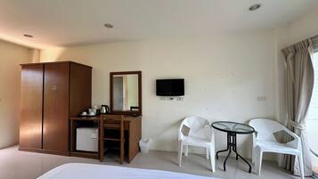 Habitación de hotel con cama, armario, escritorio con espejo, televisión y dos sillas blancas junto a una mesita.