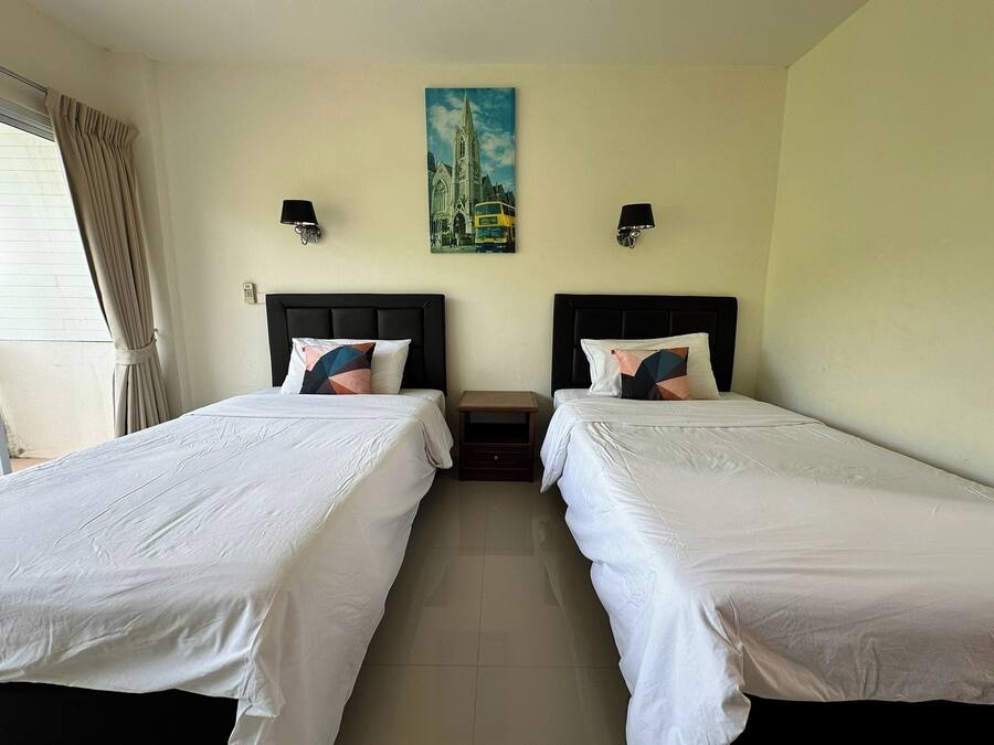 A hotel room with two single beds, a small table, and a painting of a building on the wall.