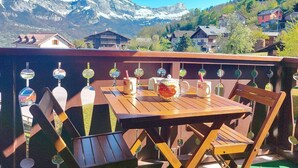 A wooden table and chairs on a balcony with a view of snow-capped mountains and houses in the background. - Beautiful apartment for 3 guests with WIFI, TV, balcony and pets allowed (Saint-gervais-les-bains)