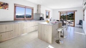Een moderne keuken met houten kastjes, een centraal eiland met barstoelen en grote ramen met uitzicht op de omgeving.