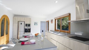 Een moderne keuken met een centraal eiland, inbouwapparatuur en een groot raam dat voor natuurlijk licht zorgt.