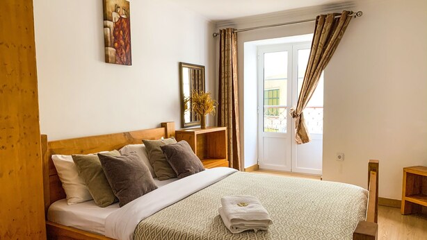 Ein Schlafzimmer mit einem hölzernen Bett, einem Bild an der Wand, einem Spiegel und einem Fenster mit Vorhängen.