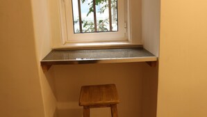 Ein kleines Fenster mit einer Holzablage und einem Hocker davor.