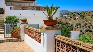A white building with terracotta pots on the balcony, a brick wall, and a view of a hilly landscape.