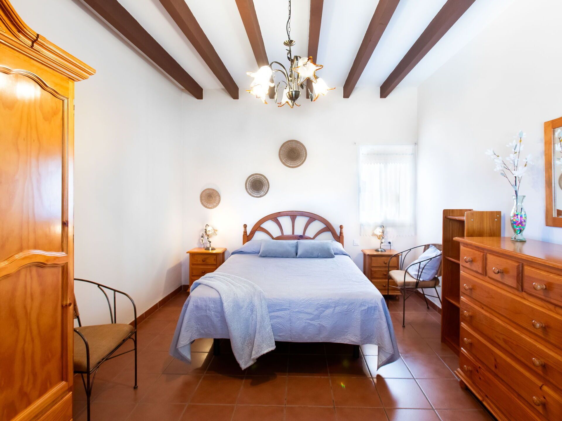 Een slaapkamer met een bed, een houten dressoir en een kroonluchter.