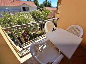A balcony with a white table and two white chairs, surrounded by a metal railing and potted plants.