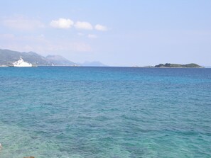 A coastal scene with a white ship in the water, a distant island, and mountains in the background.