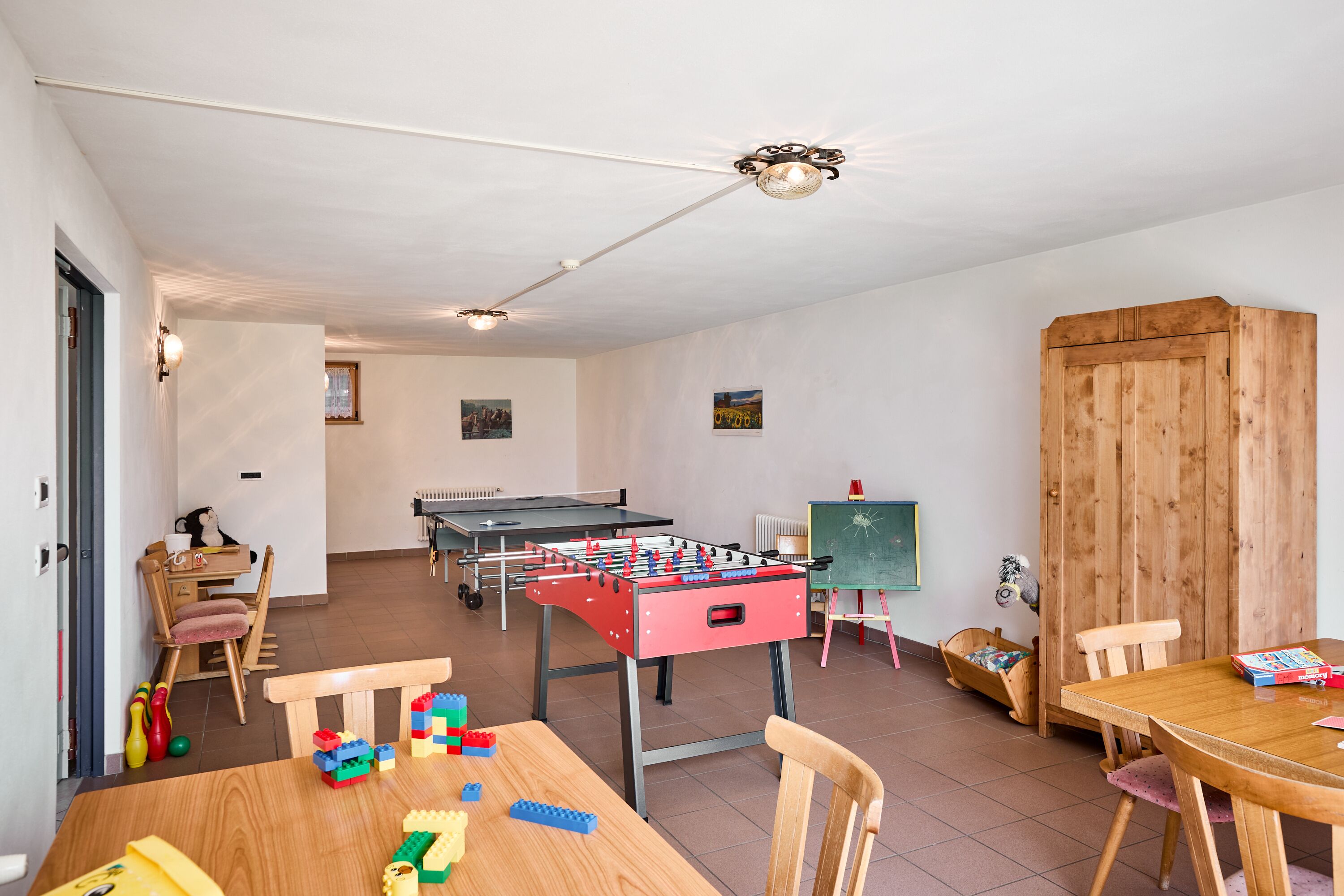 Una habitación con mesa de fútbol de mesa, mesa de ping pong y un armario de madera.