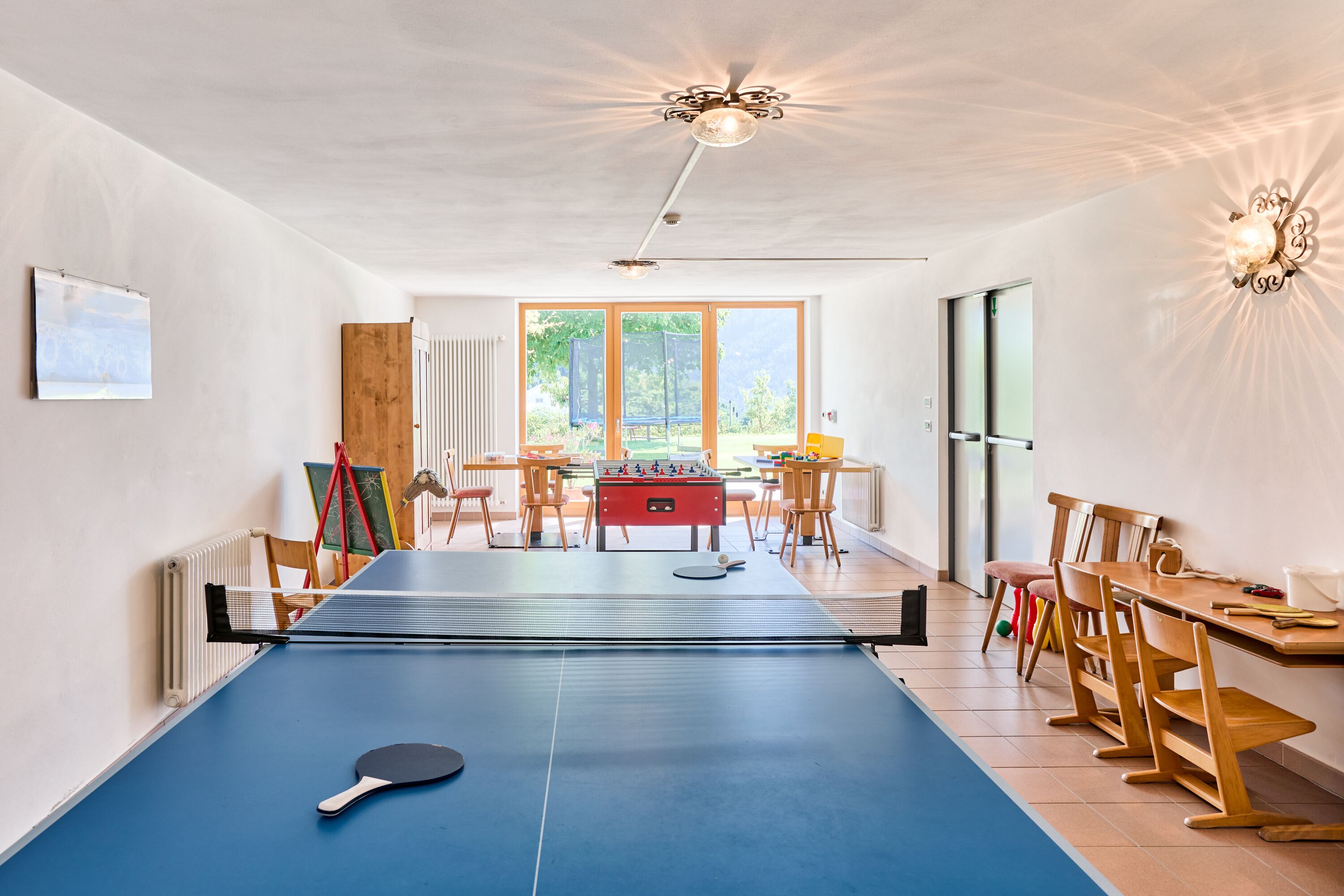 Een kamer met een tafeltennistafel, een tafelvoetbaltafel en een eethoek met houten stoelen en een tafel.