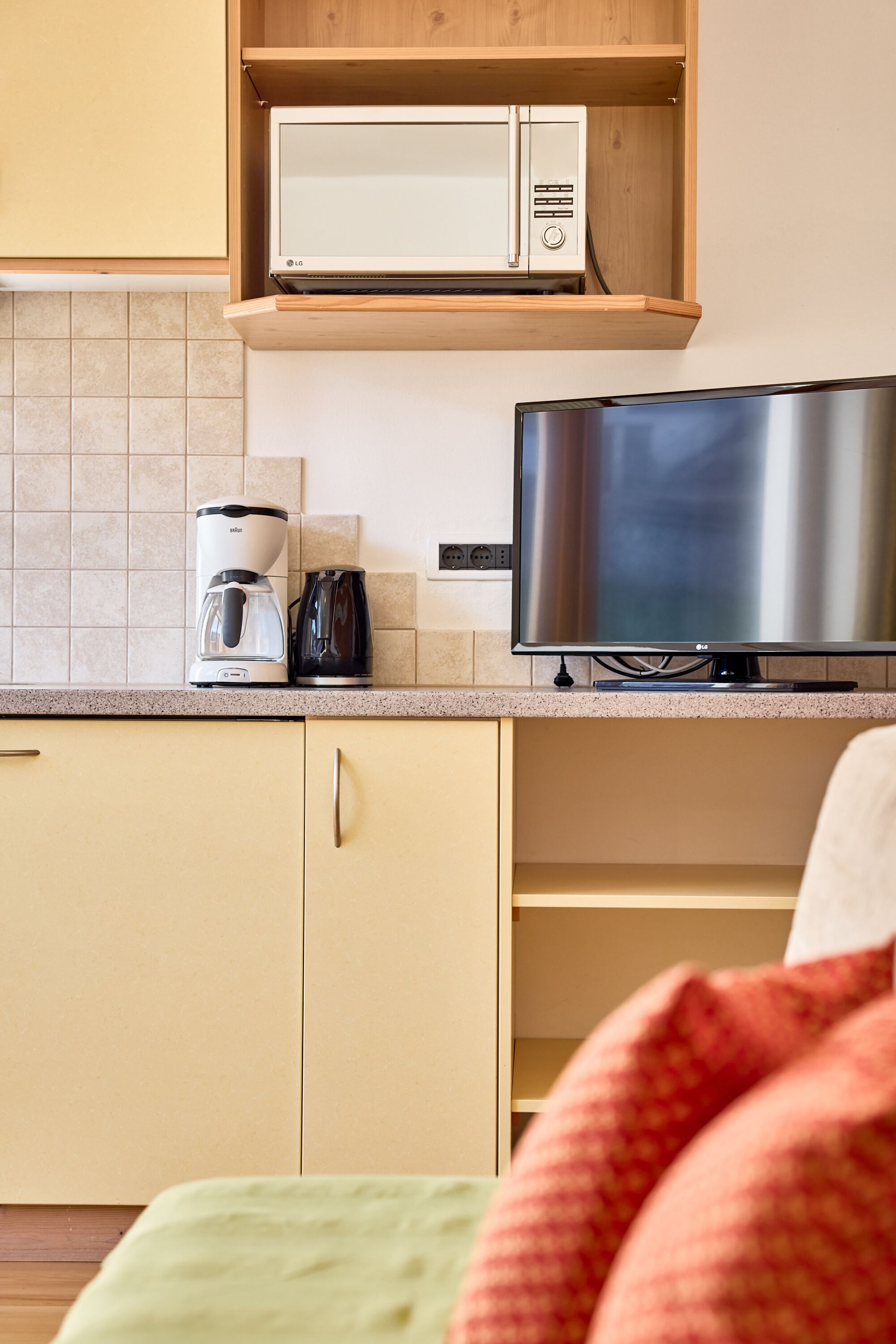 Eine Küche mit Mikrowelle, Kaffeemaschine und einem Flachbildfernseher auf einer Arbeitsfläche.