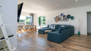 Ein geräumiges Wohnzimmer mit einer Eckcouch, einem Essbereich mit Tisch und Stühlen sowie einer Wand, die mit Tellern dekoriert ist.