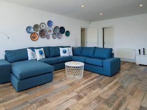 Una sala de estar moderna con un sofá seccional azul, una mesa de centro redonda y una pared decorada con varios platos.